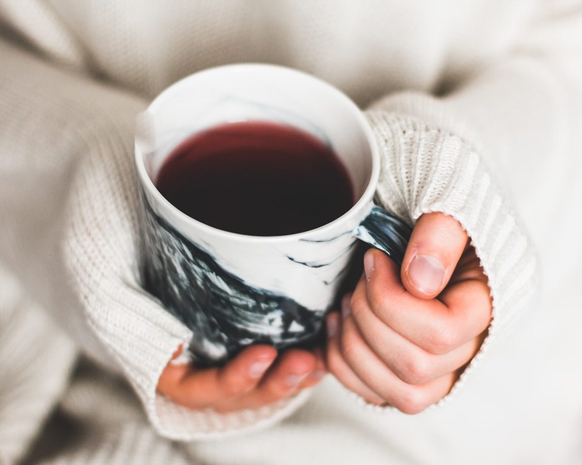 Twee hande hou 'n warm beker vas, toegedraai in 'n sagte trui